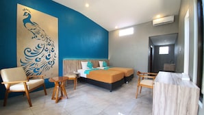 A hotel room with a large peacock mural, a bed with two bedsheets, a wooden chair, a small round table, and a marble side table.
