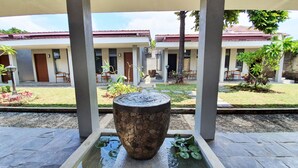 A courtyard with a stone water feature, a covered seating area, and a building with a red roof in the background.