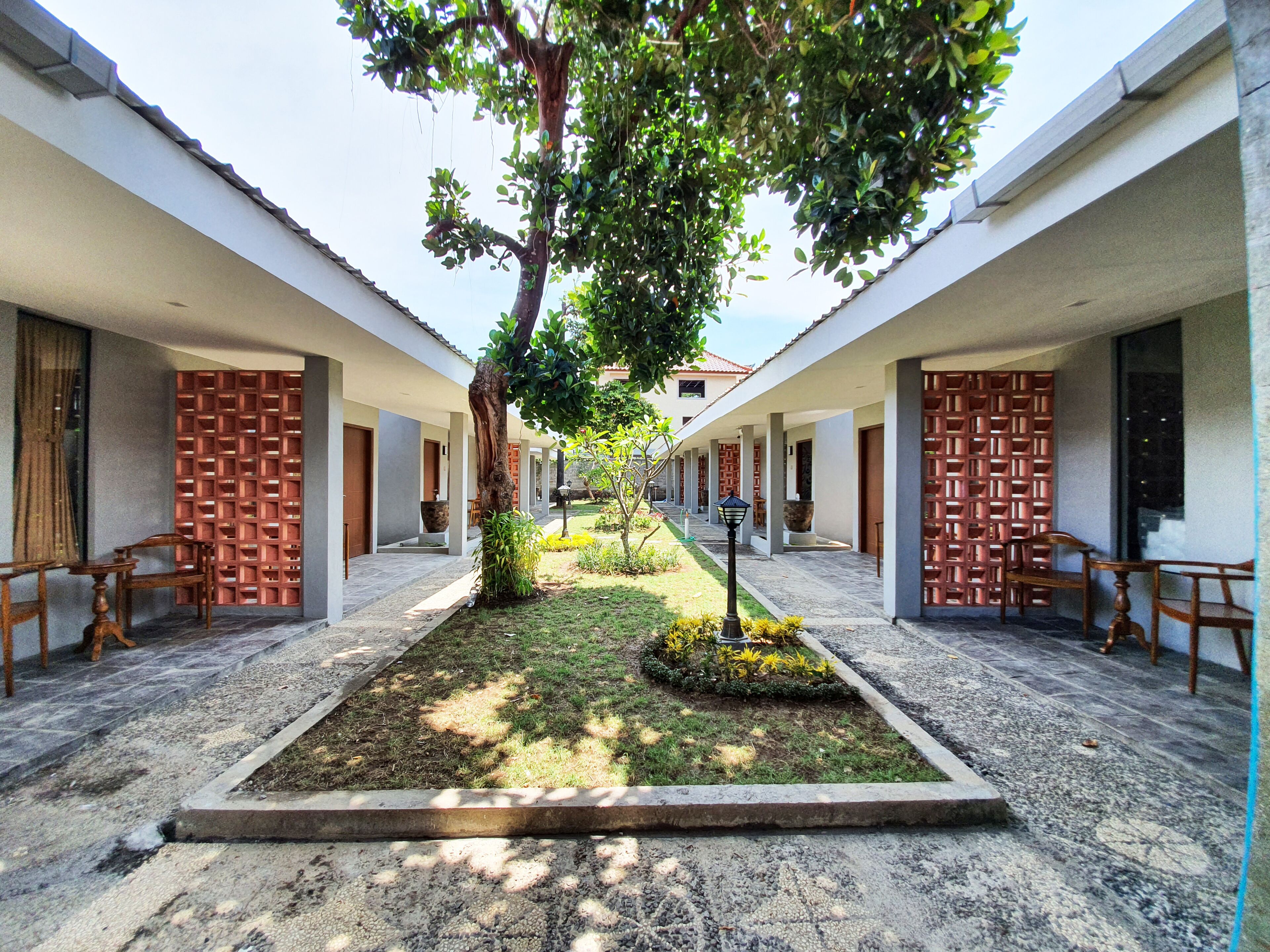 A courtyard with a central tree, surrounded by a pathway and seating areas, with buildings on either side.