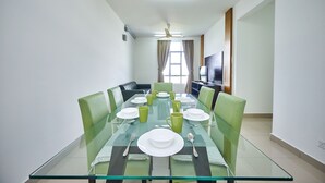 A dining area with a glass table set for six, green upholstered chairs, and a ceiling fan. - OYO Home 89748 Classic 3 Br The Arc (Cyberjaya)
