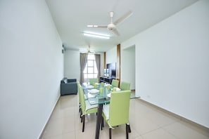 Un espace repas moderne avec une table en verre, des chaises vertes et un ventilateur de plafond.