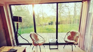 A spacious room with a large window, a wooden table, two chairs, and a floor lamp. - Panacée Guesthouses (Ronse)