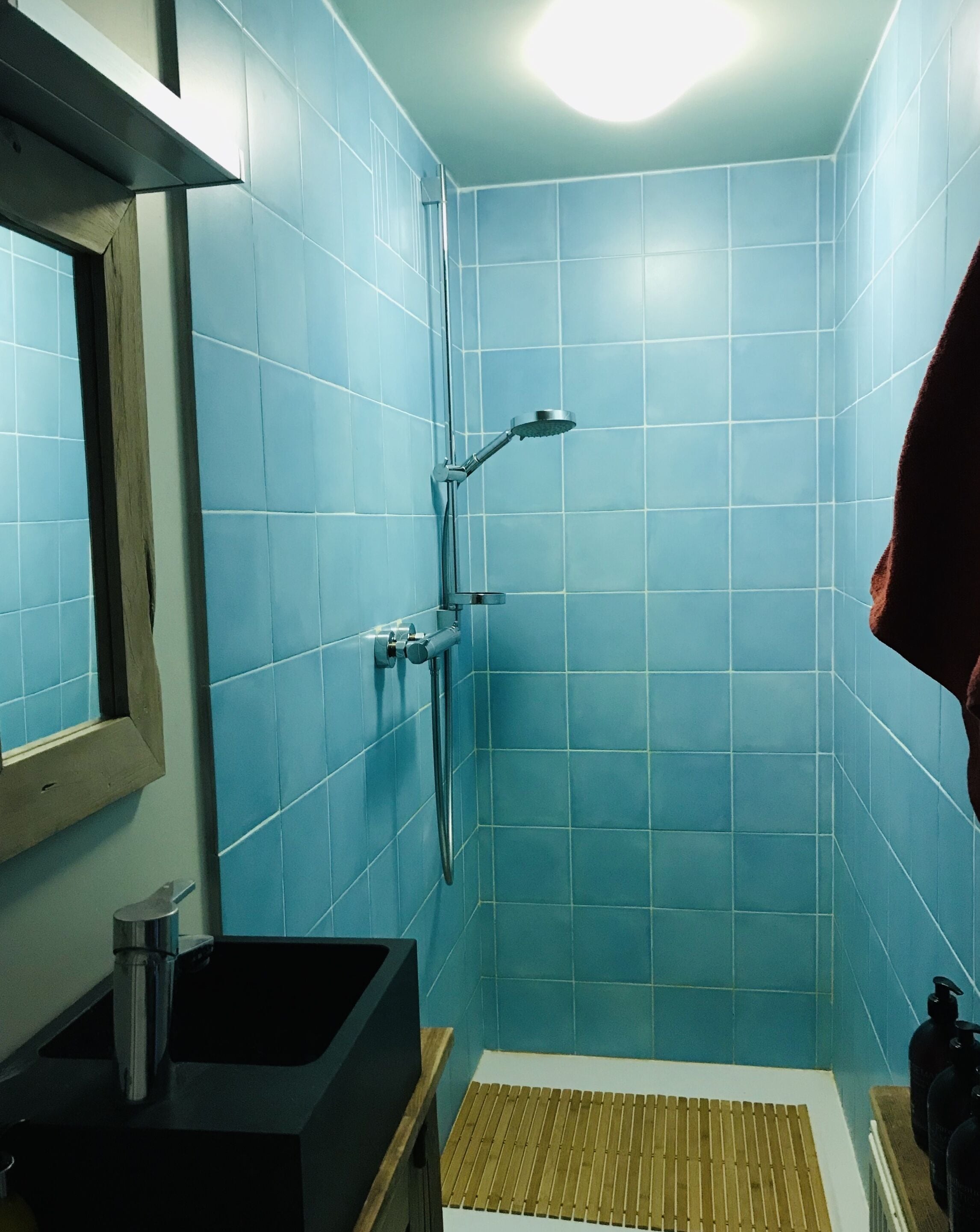 A bathroom with blue tiles, a shower, a sink, and a mirror.