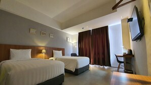 Une chambre d’hôtel avec deux lits, un bureau, une chaise, une télévision et une grande fenêtre avec des rideaux.