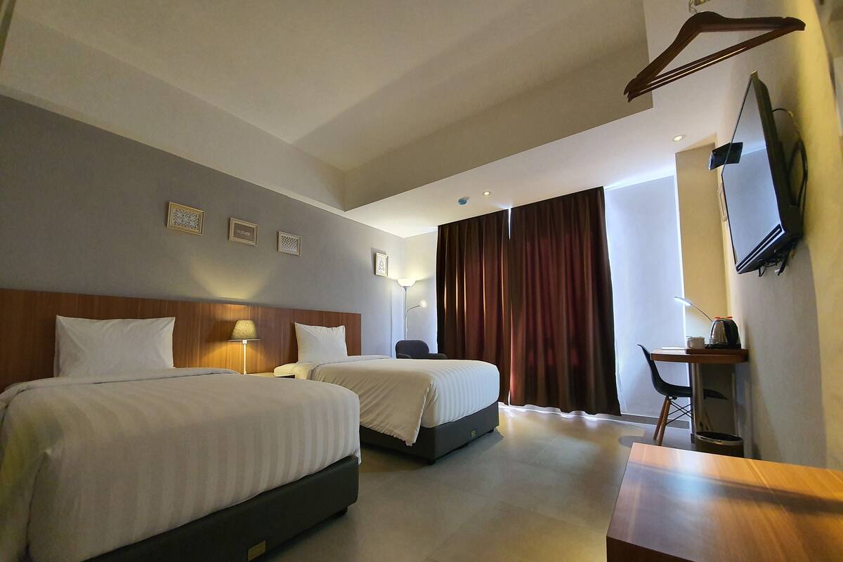 Une chambre d’hôtel avec deux lits, un bureau, une chaise, une télévision et une grande fenêtre avec des rideaux.