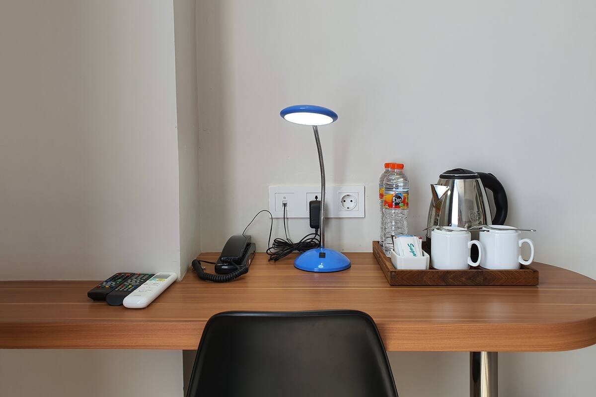 Un bureau en bois, une lampe de bureau, une bouteille d’eau, une bouilloire et deux tasses.
