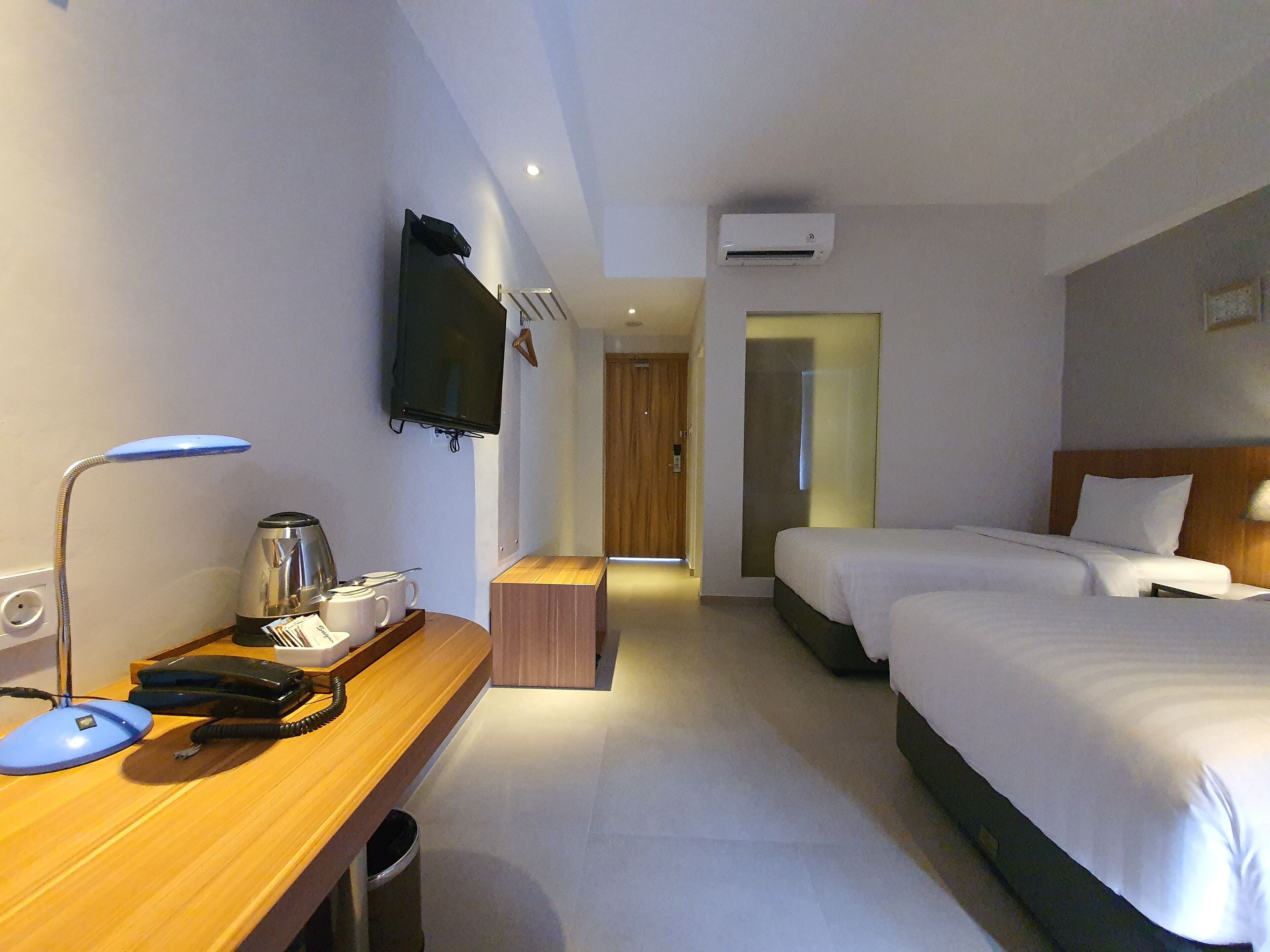 A hotel room with two beds, a desk with a telephone, a coffee maker, and a television on the wall.