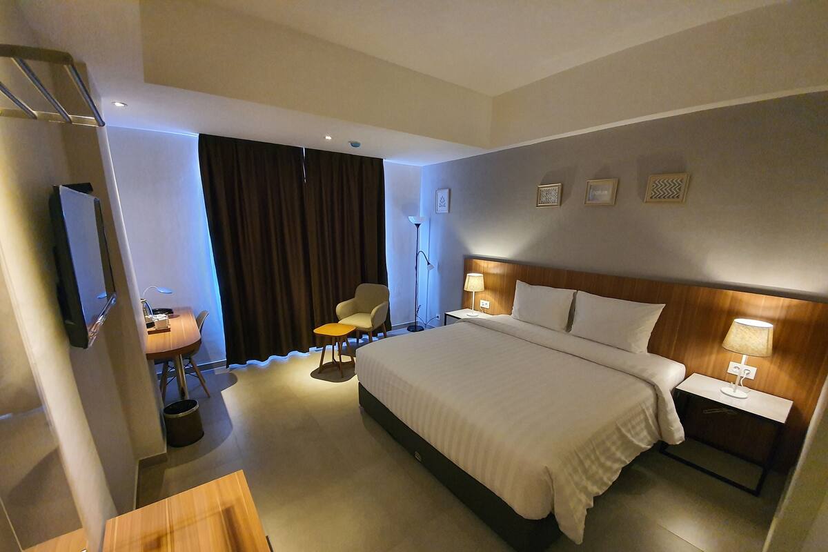 Une chambre d’hôtel avec un grand lit, un bureau, une chaise, une petite table, une lampe et un téléviseur.