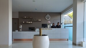 Un espace d’accueil moderne, doté d’un grand comptoir de réception, d’un élément décoratif mural et d’un grand vase placé au premier plan.