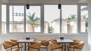 Un espace repas comprenant une table et des chaises, de grandes fenêtres offrant une vue sur les palmiers et les bâtiments.