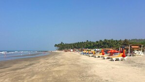 Une plage bordée de rangées de transats et de parasols, une étendue de sable et, au loin, une rangée de palmiers.