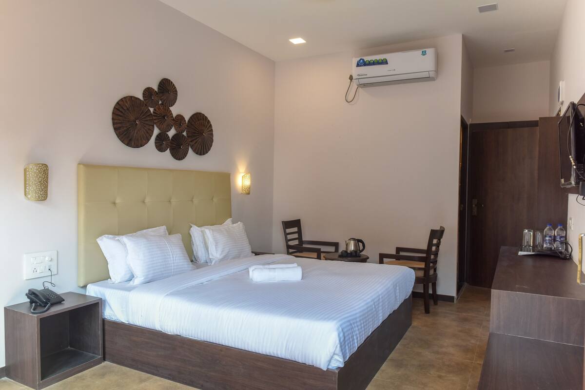 A hotel room with a bed, bedside table, lamp, wall decor, and a desk with chairs.