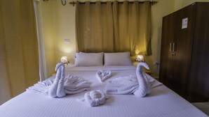 Una habitación de hotel con una cama bien tendida, dos lámparas fijadas a la pared, un armario y una cortina.