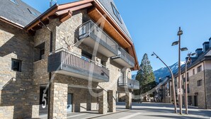 A stone building with balconies, a clear sky, and mountains in the background. - Beroia (Vielha e Mijaran)