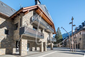 A stone building with balconies, a clear sky, and mountains in the background.