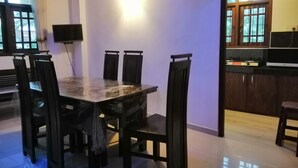 Un coin repas comprenant une table en marbre et six chaises, un téléviseur fixé au mur et une fenêtre avec des rideaux.