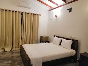 A bedroom with a bed, curtains, a bedside table, a nightstand, and a wall-mounted light.