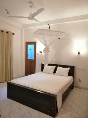 A bedroom with a bed, a ceiling fan, a door, and a wall-mounted light fixture.
