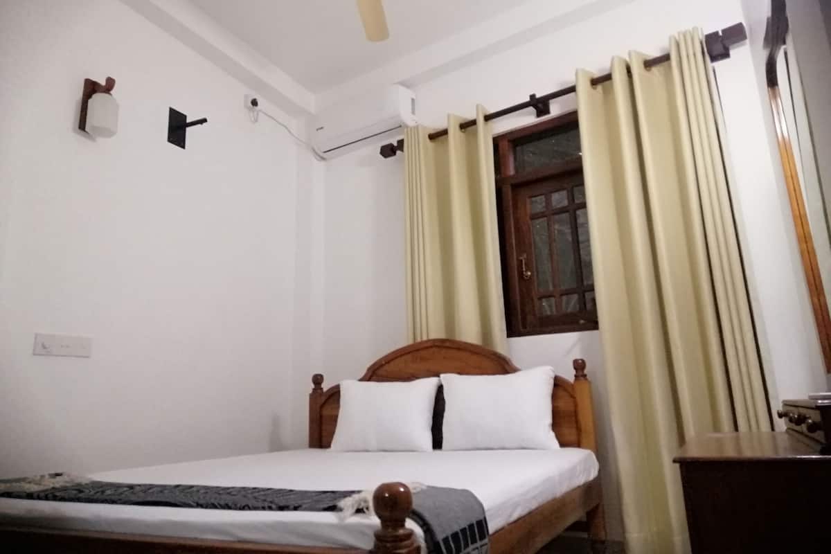 Quarto com cama de madeira, ventoinha no teto, janela com cortinas e ar condicionado fixado na parede.