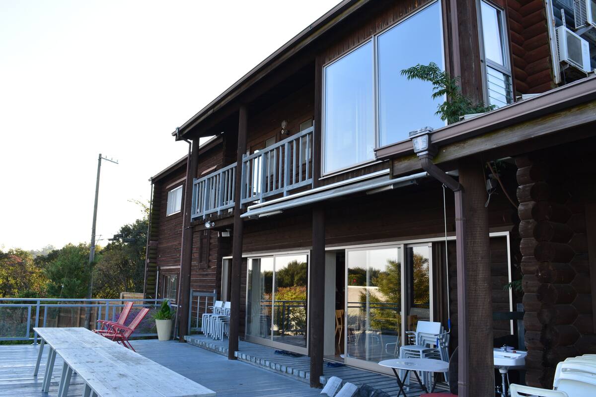 A wooden building with a balcony, large windows, and outdoor seating.