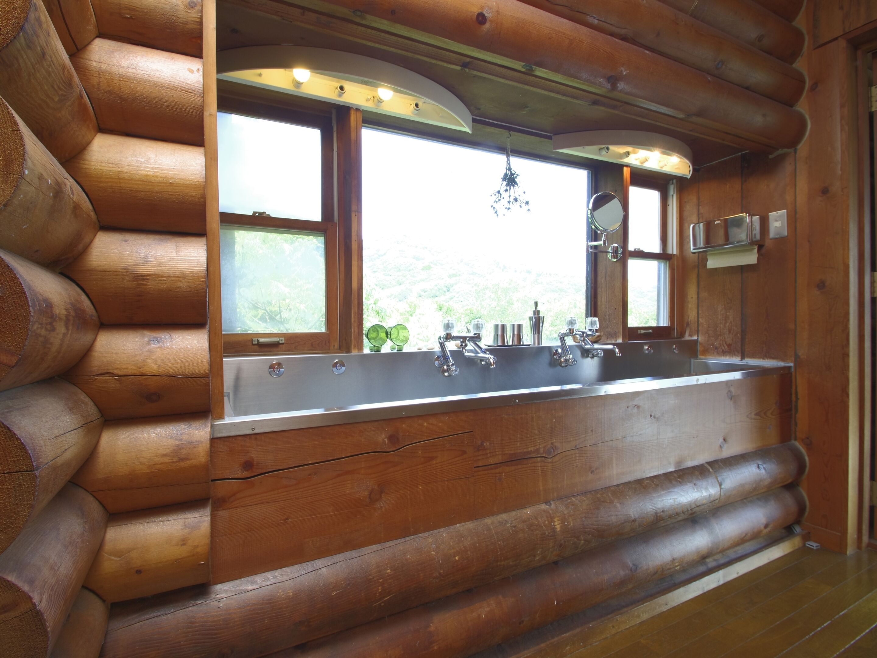 A log cabin bathroom with a large sink, wooden walls, and a view of the outdoors.