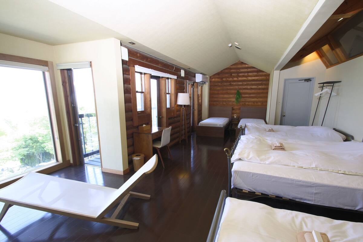 A cabin-style room with a wooden interior, a desk, two beds, and a large window.