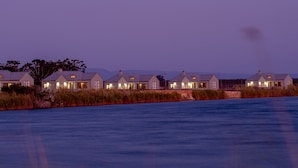 A row of modern houses with large windows and a flat roof, situated by a body of water. - L'Ermitage Quagga Lodge (Bergrivier)