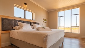 A large bed with a wooden headboard, two windows, and a view of the outdoors. - L'Ermitage Quagga Lodge (Bergrivier)