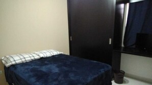 A bedroom with a bed, a wardrobe, and a small trash bin.
