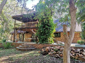 A rustic building with a wooden deck, brick walls, and a stone pathway. - Kruger Eden Lodge (Nkomazi)