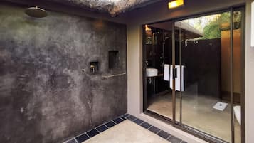 A modern bathroom with a large glass shower enclosure, a built-in sink, and a textured wall.