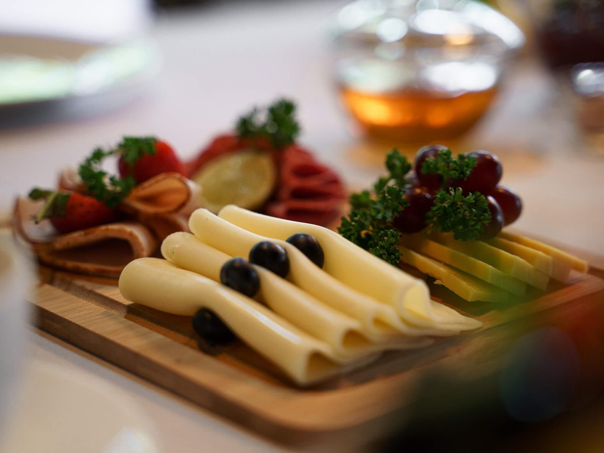 A wooden board with various cheeses, grapes, and herbs.