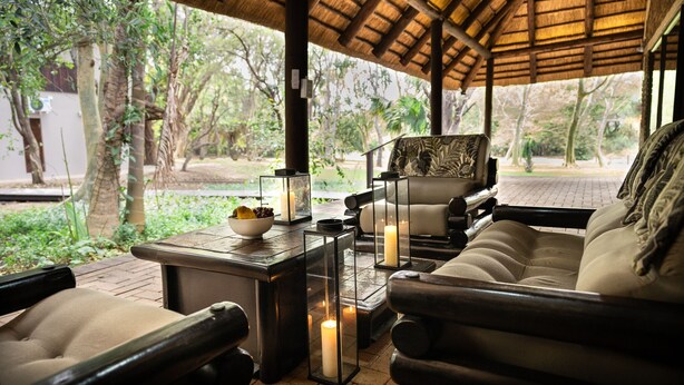 An outdoor seating area with a thatched roof, cushioned chairs, and a table with candles and fruit. - Kruger Eden Lodge (Nkomazi)