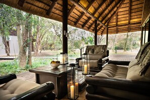 An outdoor seating area with a thatched roof, cushioned chairs, and a table with candles and fruit. - Kruger Eden Lodge (Nkomazi)