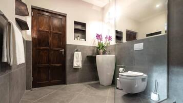 Ein modernes Badezimmer mit Holztür, grauen Fliesen, einer weißen Toilette, einem Waschbecken mit Blumen und einem Spiegel.