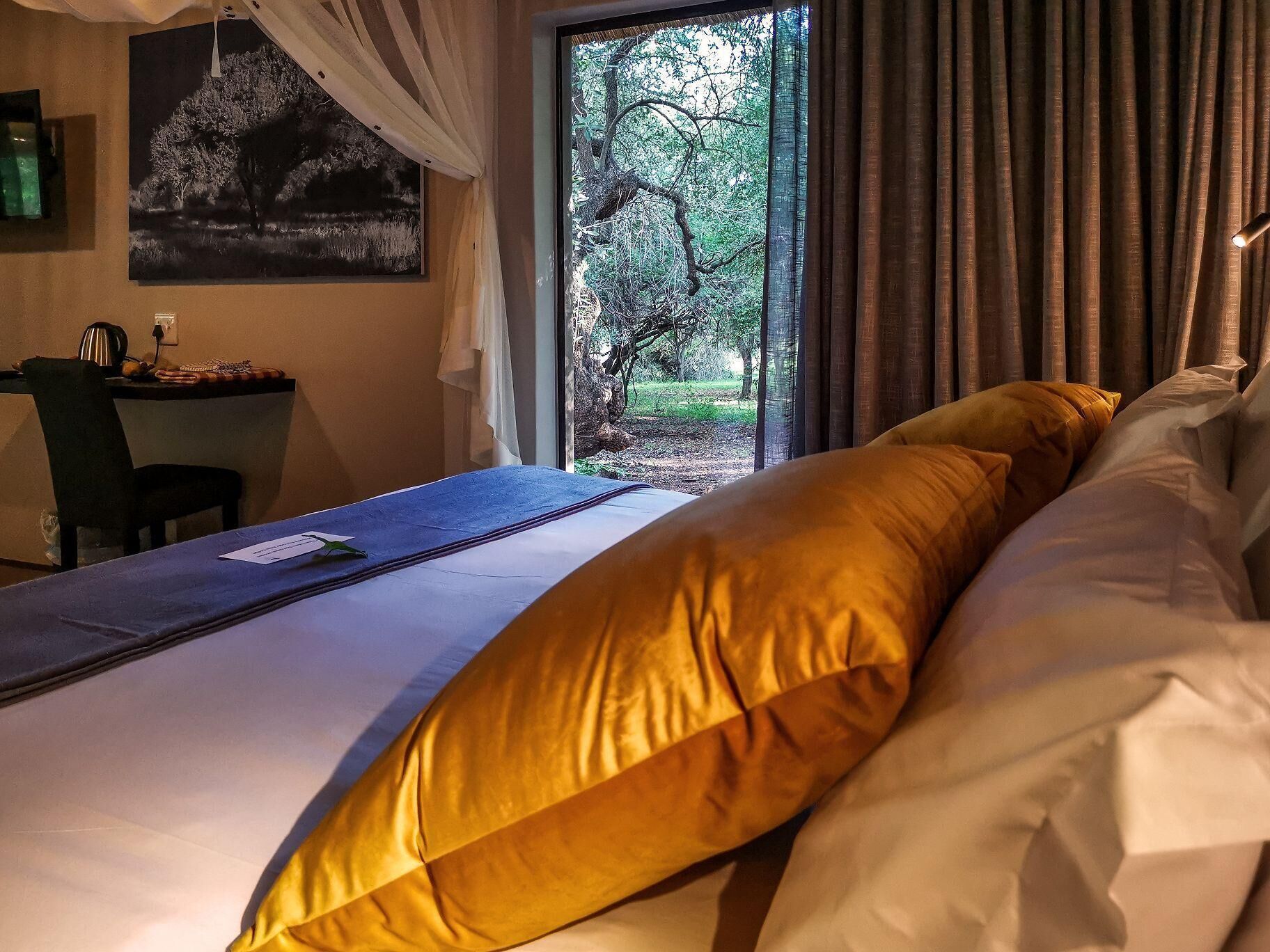 A bedroom with a bed, a desk, and a view of a forest through a window.