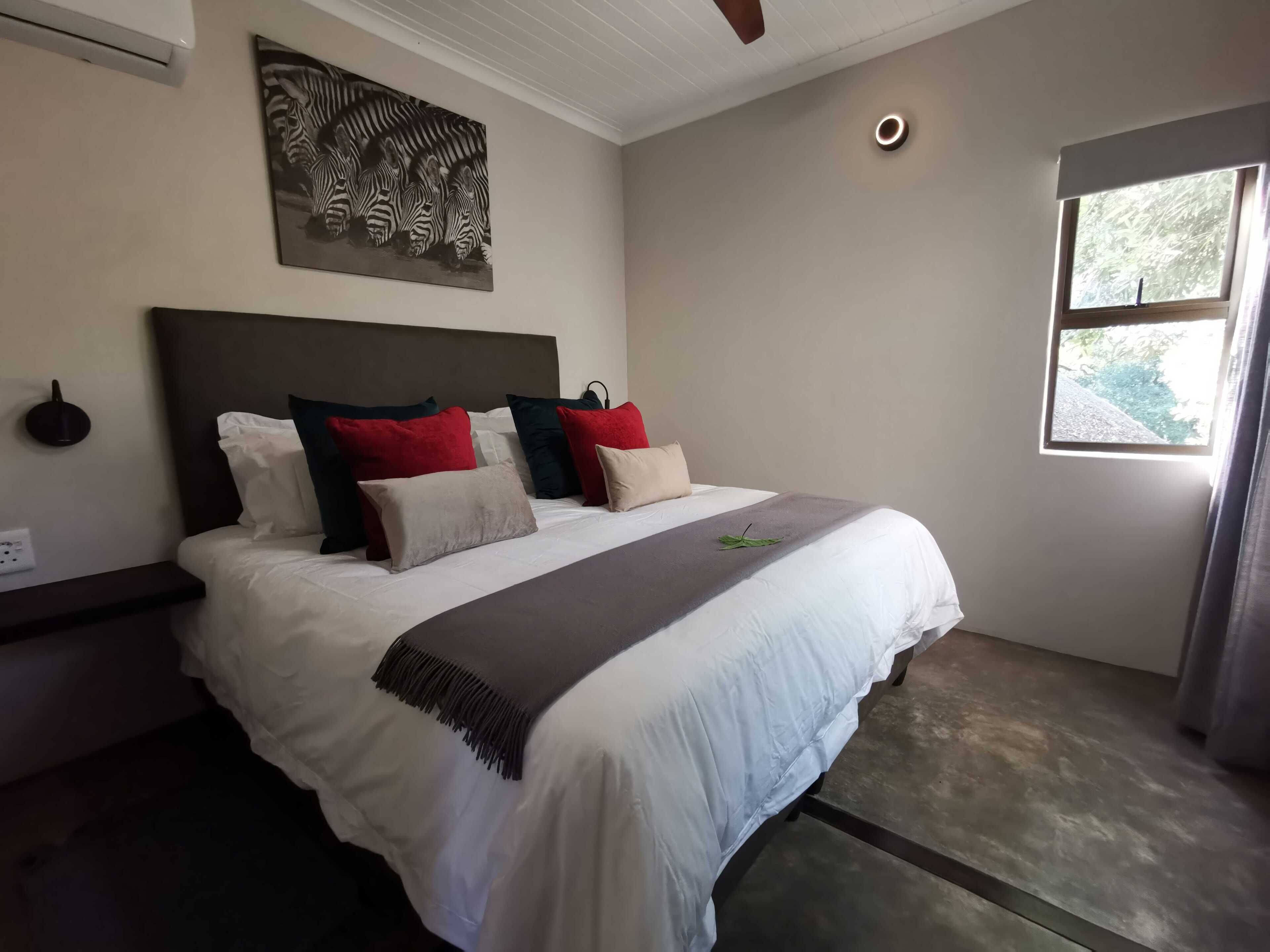 Um quarto com uma cama grande, uma obra de arte de zebra na parede, um ventilador de teto e uma janela com cortinas.