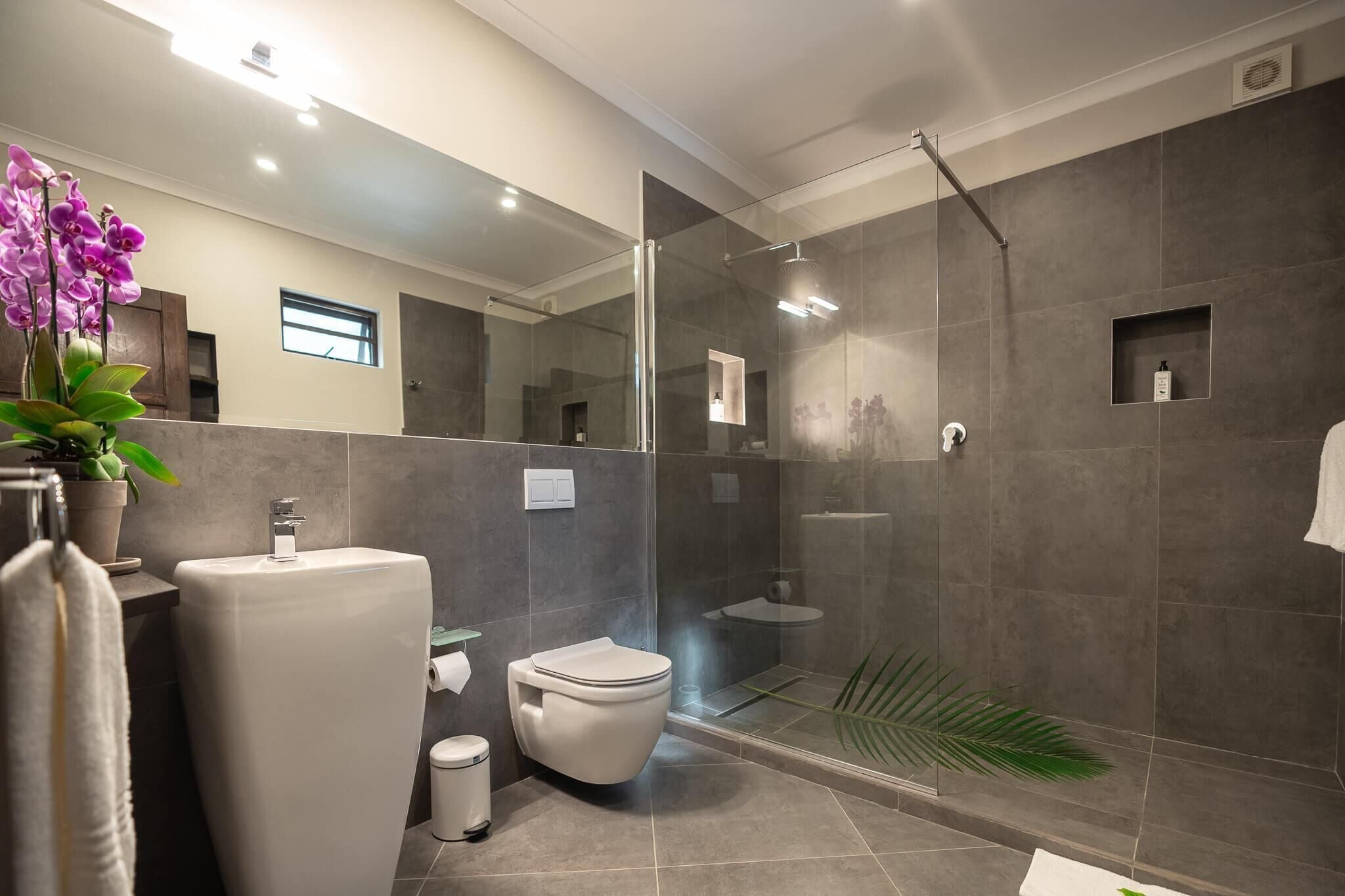 A modern bathroom with a glass-enclosed shower, a white toilet, and a sink.