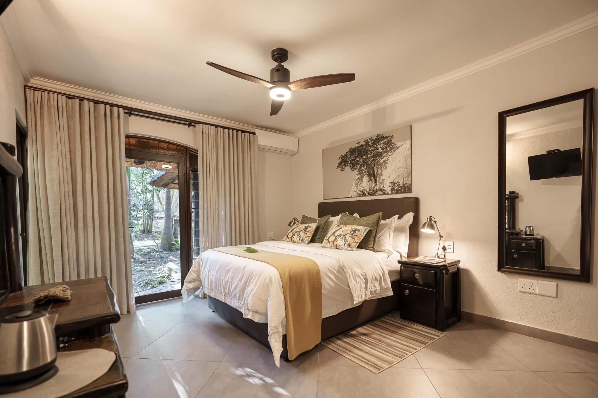 A bedroom with a bed, bedside tables, a ceiling fan, a large mirror, and a view through a glass door.