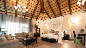 A spacious bedroom with a canopy bed, a sitting area with a sofa and coffee table, and a dining area with a table and chairs. - Kruger Eden Lodge (Nkomazi)
