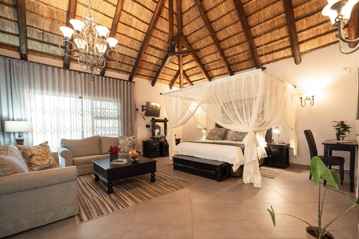 A spacious bedroom with a canopy bed, a sitting area with a sofa and coffee table, and a dining area with a table and chairs.