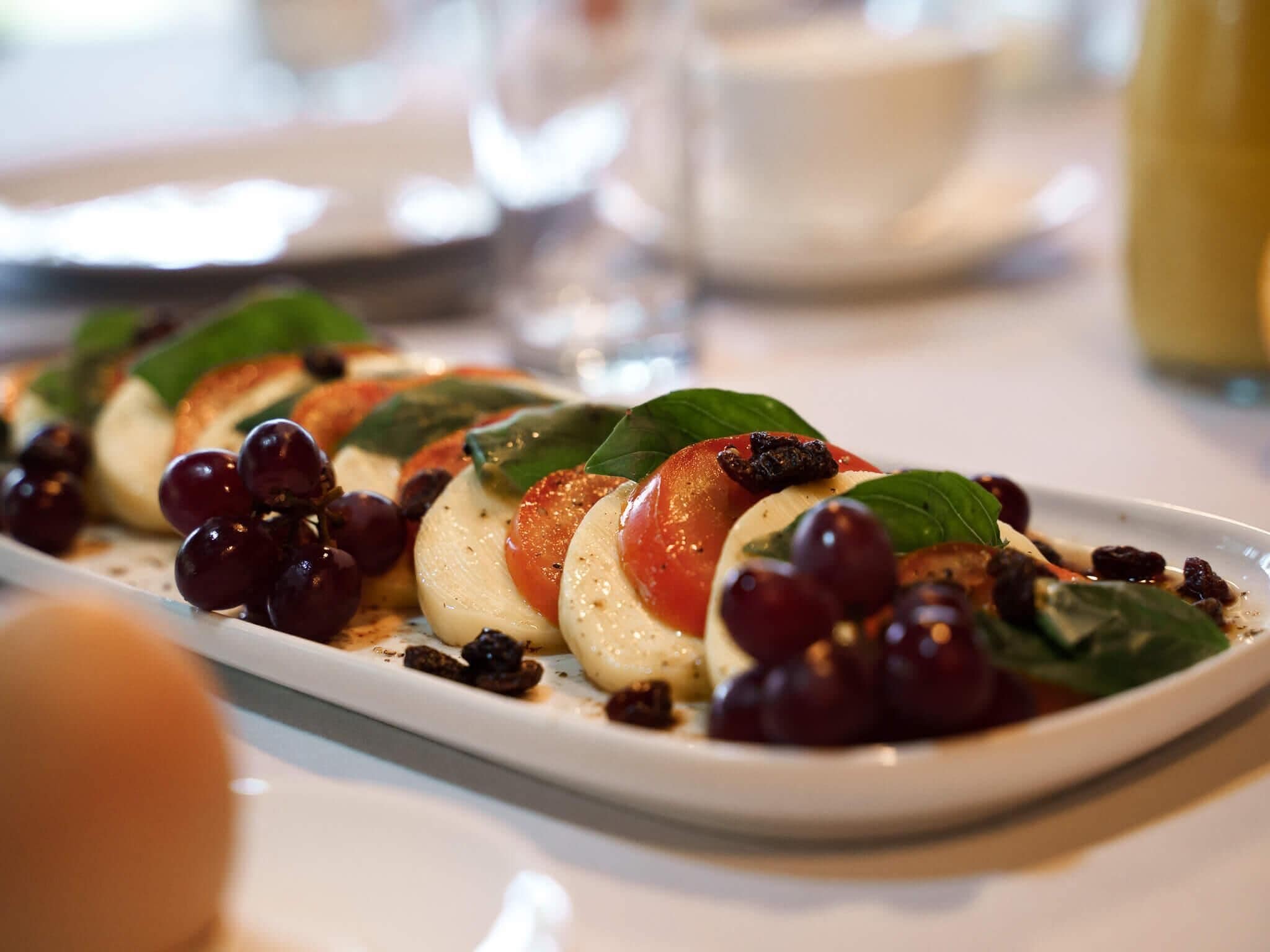 A plated dish of Caprese salad with tomatoes, mozzarella, and grapes, garnished with basil leaves.