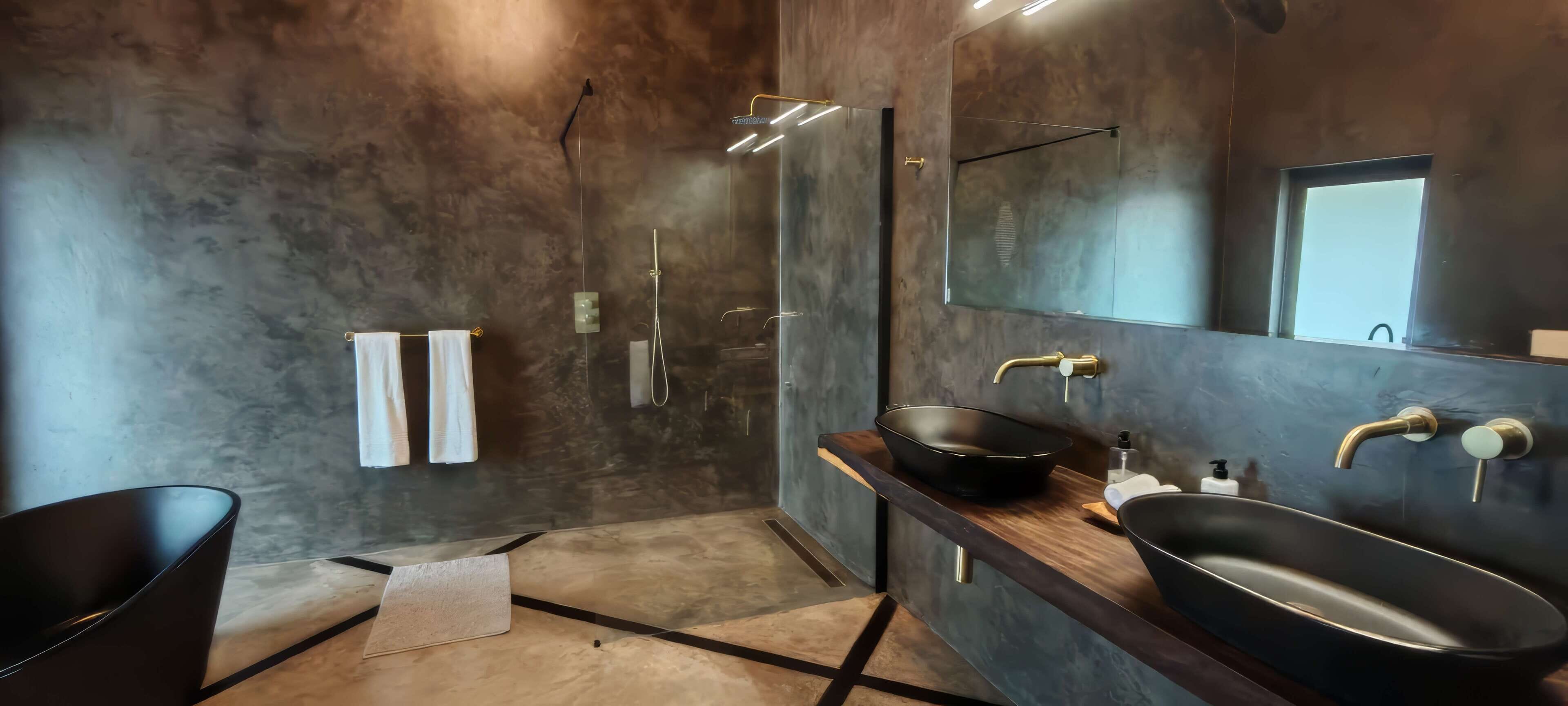 A modern bathroom with a large mirror, a black sink, and a glass-enclosed shower.
