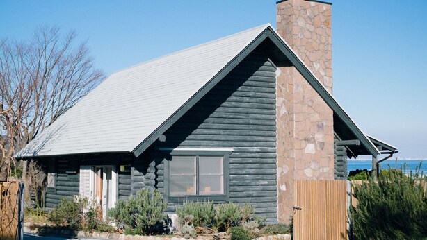 Une cabane en rondins avec une cheminée en pierre, une grande fenêtre et une cour clôturée.