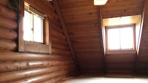 Une chambre de style rustique, avec deux fenêtres, un plafond en pente et un sol à carreaux.
