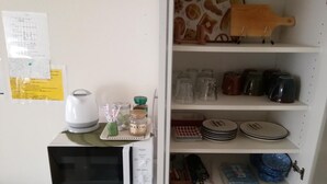 Een keuken met een magnetron, een koffiezetapparaat en een plank met borden, bekers en potjes.