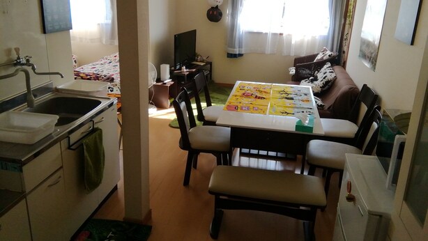 Een gezellige woonkamer met een eettafel, stoelen, een bank en een televisie. Er is een keuken met een spoelbak en kastjes.