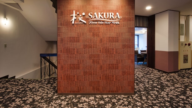 A reception area with a wooden panel displaying the name "SAKURA River Side Stay 1884".
