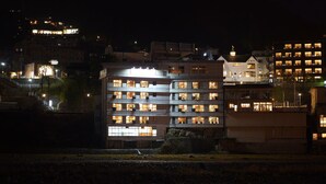 A multi-story hotel with illuminated windows, a visible staircase, and a river in the foreground.