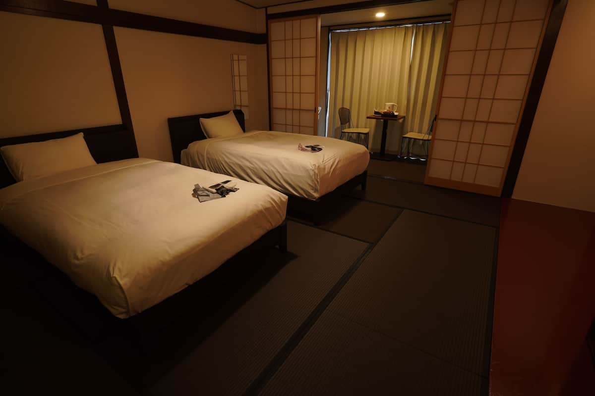 Een hotelkamer met twee bedden, een klein tafeltje met stoelen en een schuifdeur naar een balkon.
